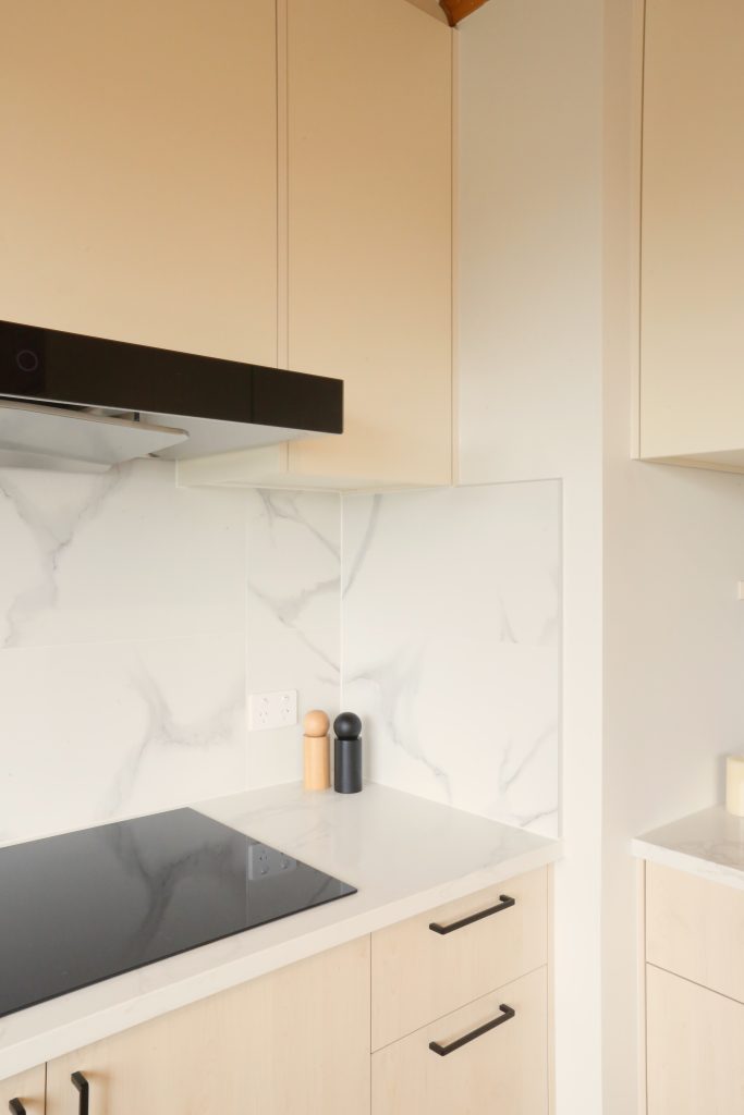 Warm woodgrain open plan kitchen with engineered stone benchtop ad marble veined splashback, kitchen renovation Auckland