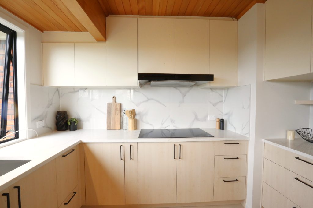 Warm woodgrain open plan kitchen with engineered stone benchtop ad marble veined splashback, kitchen renovation Auckland